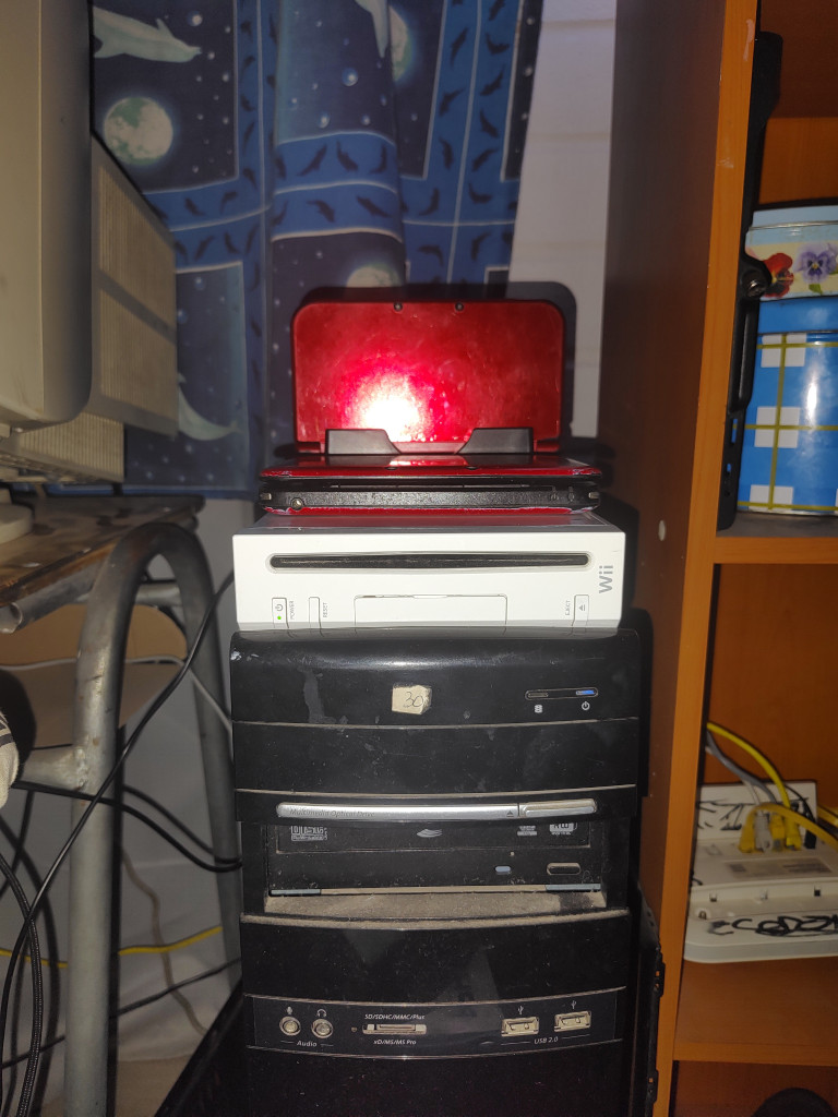 Photo of a Nintendo Wii with two Nintendo 3DS XL consoles on top over a dusty computer